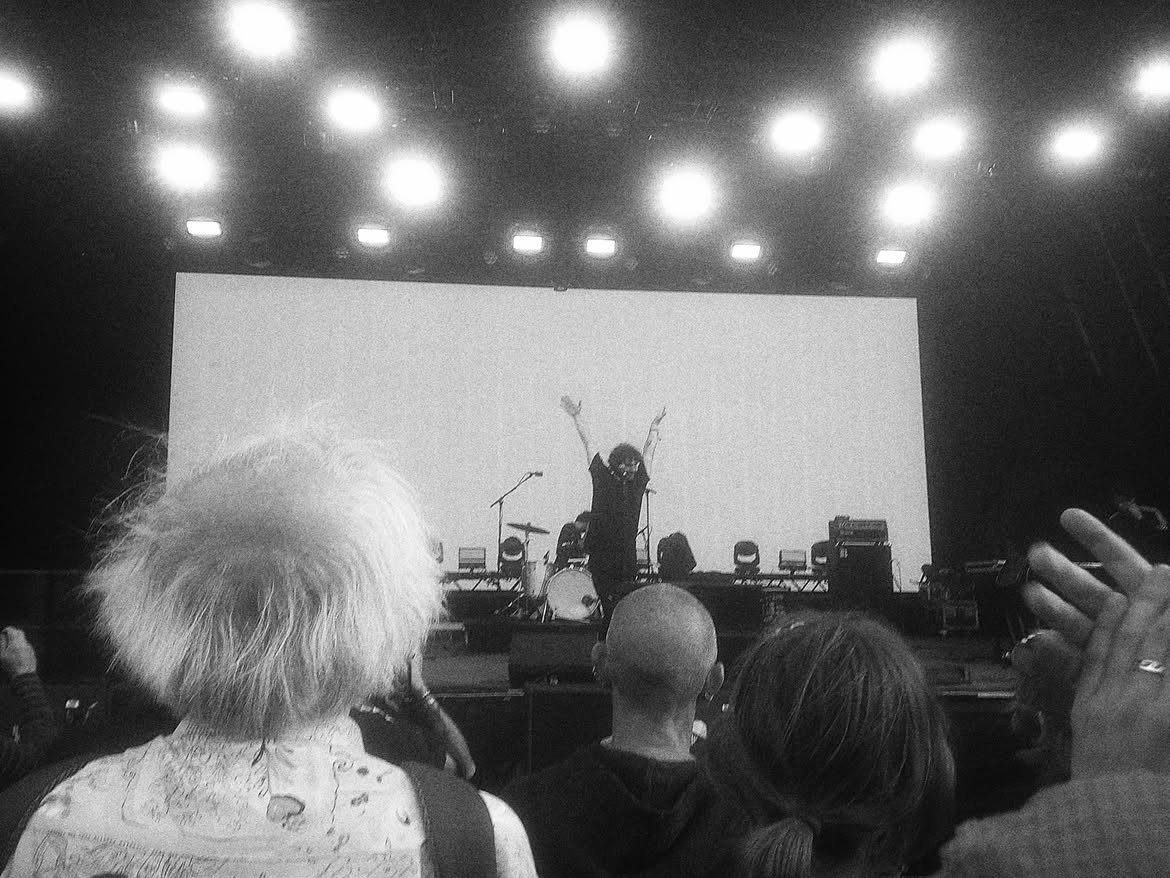 A performer with both arms raised on a big stage, seen over the crowd